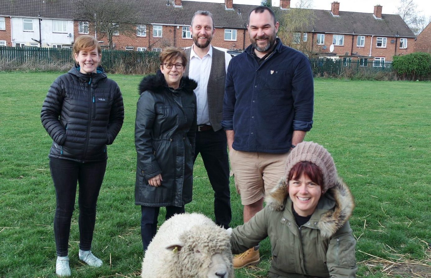 group photo of people stood with a sheep in a field