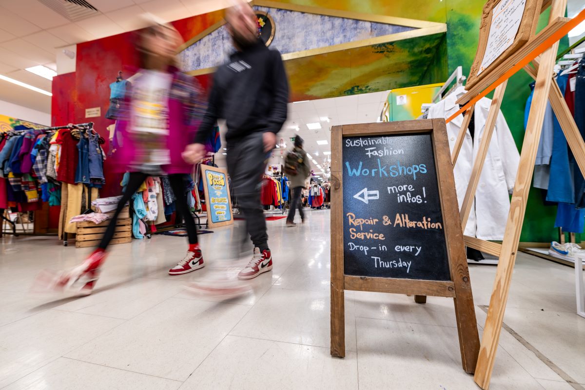 People walking past a sign for sustainable fashion workshops at Sparks community-led department store in Bristol.