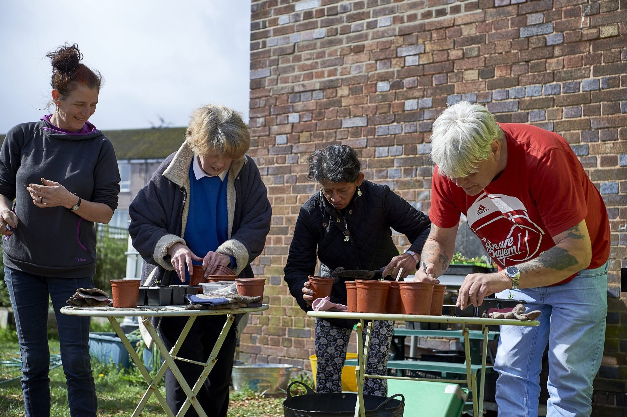Four people of different ages and backgrounds plant seeds in pots at Squash Nutrition. Four people of different ages and backgrounds plant seeds in pots at Squash Nutrition.