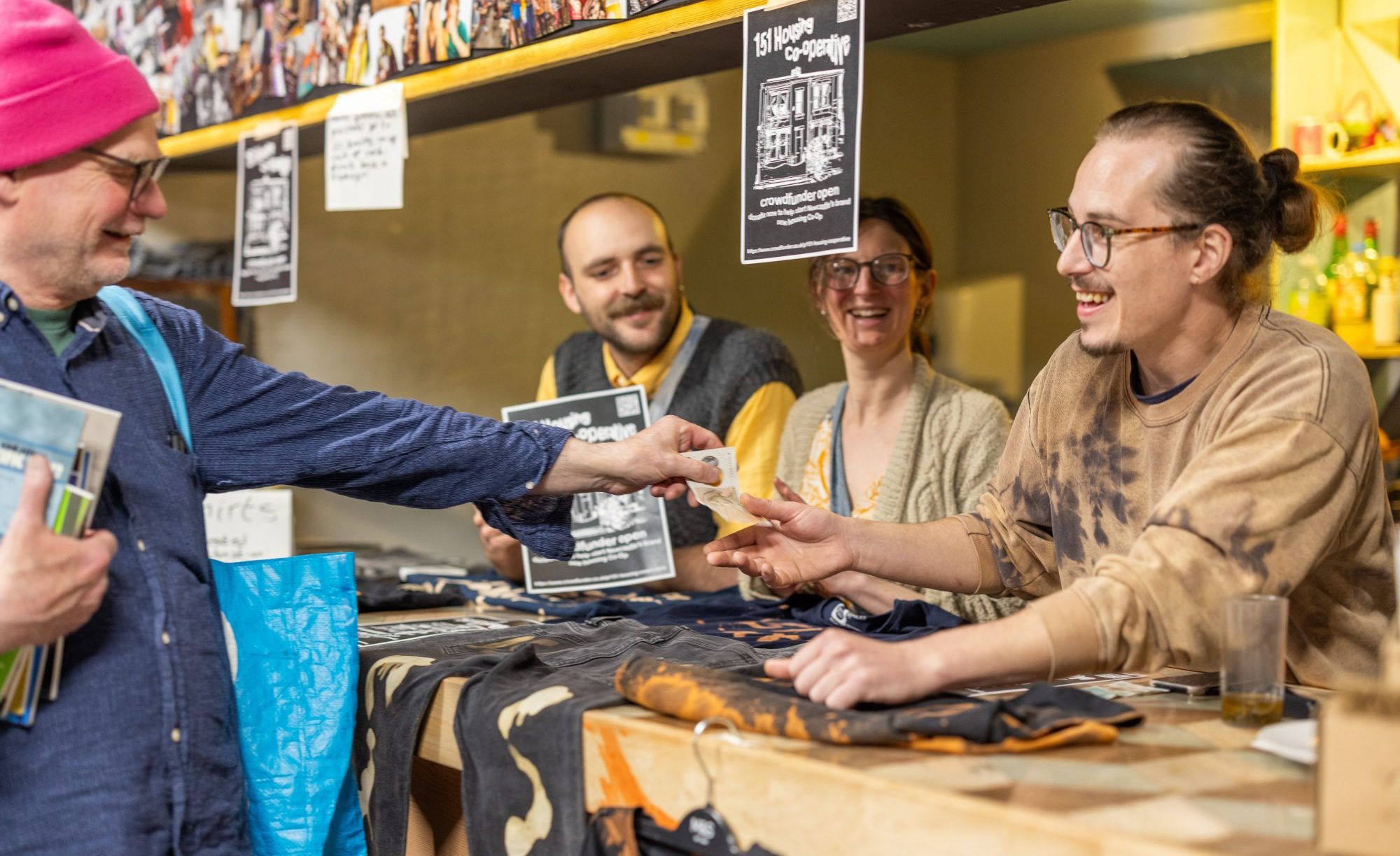 A person wearing a pink hat handing over cash to three people running a clothing stall.